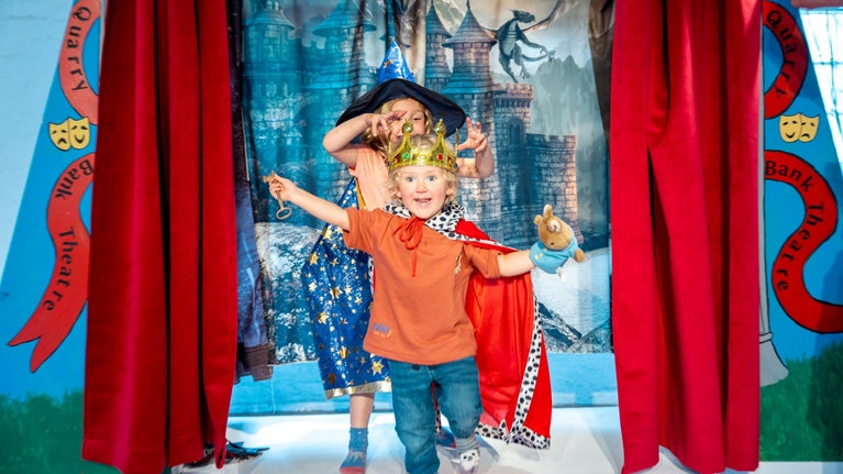 Two children walking through a red curtain on a play stage